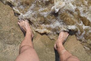 Beine Männer auf das Meer Sand in der Nähe von Meer Welle foto