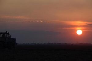 Traktor Pflügen Pflug das Feld auf ein Hintergrund Sonnenuntergang. Traktor Silhouette auf Sonnenuntergang Hintergrund foto