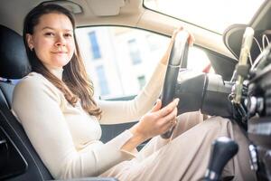 glücklich Frau Fahren ein Auto und lächelnd. süß jung Erfolg glücklich Brünette Frau ist Fahren ein Wagen. Porträt von glücklich weiblich Treiber Lenkung Wagen. foto