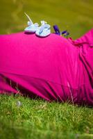 schwanger Frau Lügen auf ein Gras mit Baby Schuhe auf ihr Bauch foto