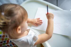 süß wenig Mädchen Gemälde mit rot Bleistift beim heim. kreativ Spiele zum Kinder. bleibe beim Zuhause Unterhaltung foto