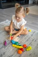 süß wenig Kleinkind Mädchen spielen beim Zuhause mit Öko hölzern Spielzeuge. glücklich Kind Schneiden Gemüse und Früchte mit Spielzeug Messer. das Kind spielen lehrreich Spiele. foto