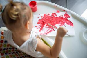 süß wenig Mädchen Gemälde mit Bürsten beim heim. kreativ Spiele zum Kinder. bleibe beim Zuhause Unterhaltung foto