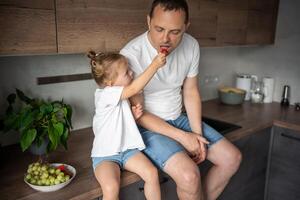 süß wenig Mädchen und ihr gut aussehend Papa sind Essen Obst im modern Küche. gesund Essen. foto