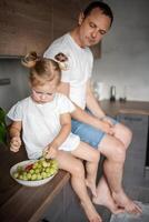 süß wenig Mädchen und ihr gut aussehend Papa sind Essen Obst im modern Küche. gesund Essen. foto