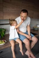 süß wenig Mädchen und ihr gut aussehend Papa sind Essen Obst im modern Küche. gesund Essen. foto