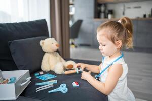 wenig Mädchen spielen Arzt mit Spielzeuge und Teddy Bär auf das Sofa im Leben Zimmer beim Zuhause foto