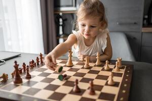 wenig Mädchen spielen Schach beim das Tabelle im Zuhause Küche. das Konzept früh Kindheit Entwicklung und Bildung. Familie Freizeit, Kommunikation und Erholung. foto