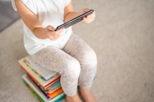 Kind sitzt auf ein Stapel von Kinder- Märchen Bücher und Uhren Cartoons auf Smartphone foto