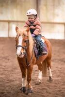 wenig Kind Reiten Lektion. Drei Jahre alt Mädchen Fahrten ein Pony und tut Übungen. hoch Qualität Foto