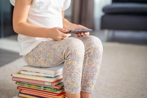 wenig Mädchen sitzt auf ein Stapel von Kinder- Märchen Bücher und mit ihr Smartphone foto