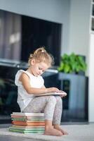 wenig Mädchen ist Sitzung auf Stapel von Kinder- Bücher und Blättern durch ein Buch mit Bilder von Fee Erzählungen foto