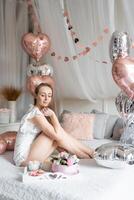 schön jung Mädchen beim Zuhause auf das Bett im das Morgen genießen Valentinsgrüße Tag Feier mit Herz geformt Luftballons. hoch Qualität Foto