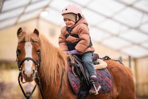 wenig Kind Reiten Lektion. Drei Jahre alt Mädchen Fahrten ein Pony und tut Übungen. hoch Qualität Foto