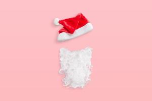 Weihnachtsmann-Hut und Bart auf pastellrosa Schreibtisch, minimale Komposition foto