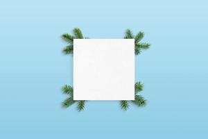 leeres papier verziert mit weihnachtsbaumzweigen auf pastellblauer oberfläche. Grußkartenmodell foto
