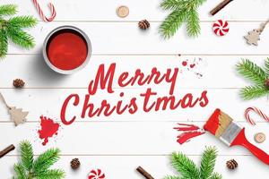 Frohe Weihnachten mit Pinsel auf weißer Holzoberfläche gemalt und von Weihnachtsschmuck umgeben. Grußkarte foto