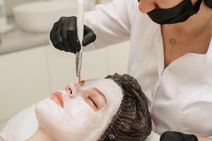 Nahansicht von weiblich Fachmann Kosmetikerinnen Hände bewirbt sich Maske zu Patienten Gesicht zum Gesichts- Haut Pflege. foto