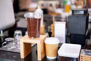 verbrannt braun Kaffee Pulver im ein klar Plastik Kaffee Tasse sitzt auf ein hölzern Zähler in der Nähe von das Kassierer, zu Anzeige ein Stichprobe von das Kaffee Laden Fan-Shop. foto