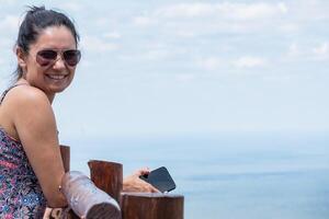 Latina Tourist Mädchen Nachdenken das Aussicht von ein hoch Standpunkt. sie hat Brille und ein Zelle Telefon im ihr Hand. foto