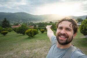 jung Wanderer nehmen ein Selfie Porträt beim das oben von ein Standpunkt. glücklich Kerl lächelnd beim das Kamera. wandern, Sport, Reise und Technologie Konzept. hell Filter. foto