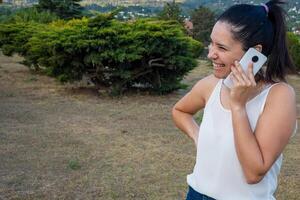 Latein Frau mit ihr Zelle Telefon im ein Park. foto