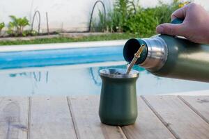 jung Mann Trinken Kamerad im das Morgen im Vorderseite von das Schwimmbad. foto