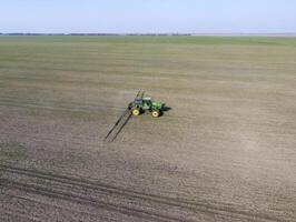 Traktor mit aufklappbar System von Sprühen Pestizide. düngen mit ein Traktor, im das bilden von ein Aerosol, auf das Feld von Winter Weizen. foto