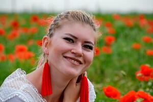 blond jung Frau im rot Rock und Weiß Shirt, rot Ohrringe ist im das Mitte von ein Mohn Feld. foto