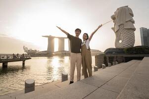 Merlion Brunnen im Vorderseite von das Yachthafen Bucht Sand mit jung asiatisch Paar von Liebe Tourist. foto