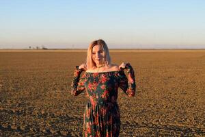 Frau im ein gepflügt Feld im ein rot schwarz Kleid auf ein Sonnenuntergang Hintergrund. foto