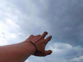 des Mannes Hand erreichen aus zum etwas von das wolkig Himmel foto