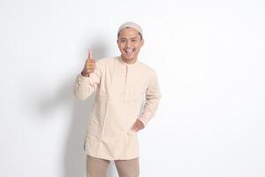 Porträt von attraktiv asiatisch Muslim Mann im koko Hemd zeigen Daumen hoch, gut Job Hand Geste. die Genehmigung Konzept. isoliert Bild auf Weiß Hintergrund foto
