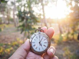 schließen oben von Jahrgang Tasche Uhr im Frau Hand mit Wald im das Sonnenuntergang Zeit wie Hintergrund. foto