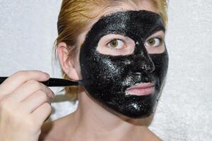 Mädchen im ein kosmetisch schwarz Maske. Reinigung Maske von Aspirin und aktiviert Kohlenstoff. schwarz kosmetisch Gesicht Maske. foto