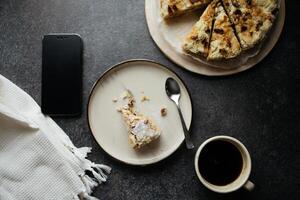 haben Mahlzeiten mit Smartphone. oben Aussicht von gebissen Stück von Kuchen auf Platte, ganze Kuchen und Tasse von schwarz Kaffee foto