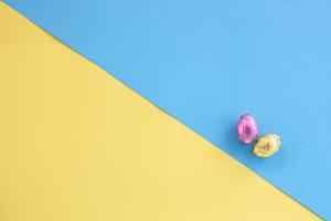 oben Aussicht von Rosa und Gold Schokolade Ostern Eier auf diagonal Gelb und Blau Hintergrund foto