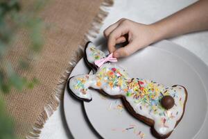 Hand von Kind Putten Bogen auf Ohr von gebacken Ostern Hase Lebkuchen Plätzchen mit multi farbig Zucker Sträusel foto