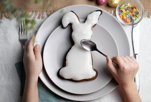 oben Aussicht von Hase geformt Lebkuchen Plätzchen. Hände von Kind dekorieren Keks mit Glasur auf Ostern Ferien foto