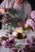 ein Frau gießt Tee von ein Silber Teekanne, Hintergrund von Rosa Sakura Blumen, Ostern foto