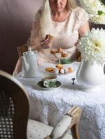 mittleren Alters blond Frau Essen Krapfen und Trinken Tee zum Frühstück, foto