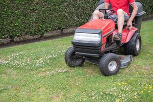 Rasen Mäher mäht das Gras, ein mittleren Alters männlich Gärtner funktioniert auf ein Mini Traktor foto