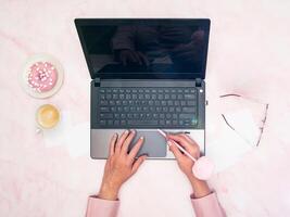 Büro Arbeiter im ein Rosa Hemd sitzt beim ein Laptop, oben Ansicht, als nächstes zu ein Tasse von Kaffee foto