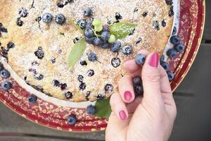 ein Frau Hand dekoriert ein frisch Kuchen mit Blaubeeren, ruckeln beim Zuhause, Essen foto