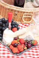 Sommer- Picknick auf ein Grün Rasen mit rot Wein, Käse und frisch Beeren, Trauben foto