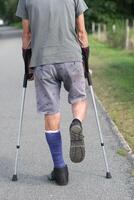 ein Mann mit ein gebrochen Bein ist Gehen Nieder das Straße, auf seine links Bein er hat ein Besondere Stiefel zum Gehen foto