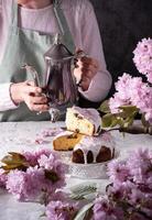 ein Frau gießt Tee von ein Silber Teekanne, Hintergrund von Rosa Sakura Blumen, Ostern foto