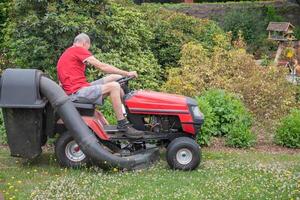 Rasen Mäher mäht das Gras, ein mittleren Alters männlich Gärtner funktioniert auf ein Mini Traktor foto