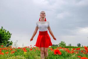 blond jung Frau im rot Rock und Weiß Shirt, rot Ohrringe ist im das Mitte von ein Mohn Feld. foto