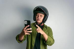 Erwachsene asiatisch Mann verwirrend wann suchen zu seine Handy während tragen Motorrad Helm foto